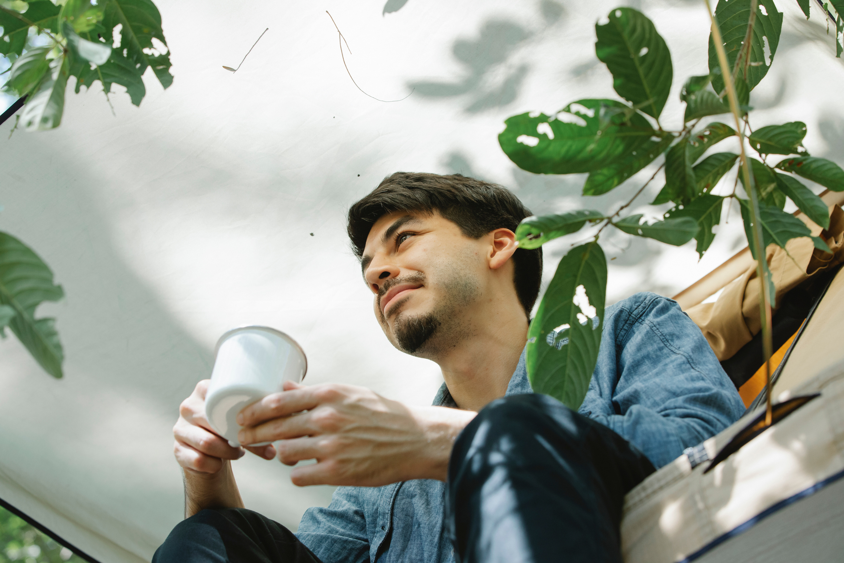 Smiling young man drinking coffee in camp tent on sunny day